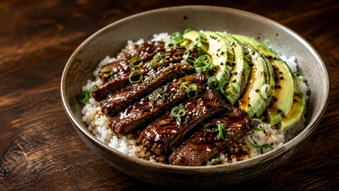 Weitwinkelaufnahme einer von Teriyaki inspirierten Rindfleisch-Reisschale mit Avocado, glasierter Ribeye-Streifen, japanischem Reis, Sesam, Frühlingszwiebeln und schwarzem Trüffelöl.